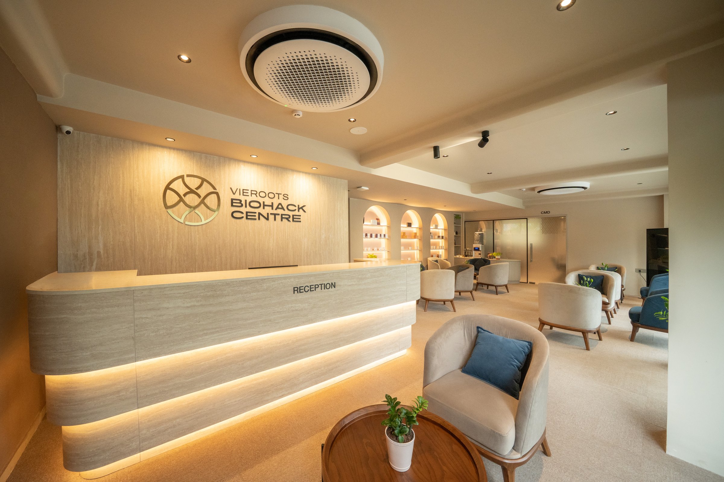 The Centre, reception desk with Vieroots Biohack Centre wordmark, warm travertine and oak, ambient evening light